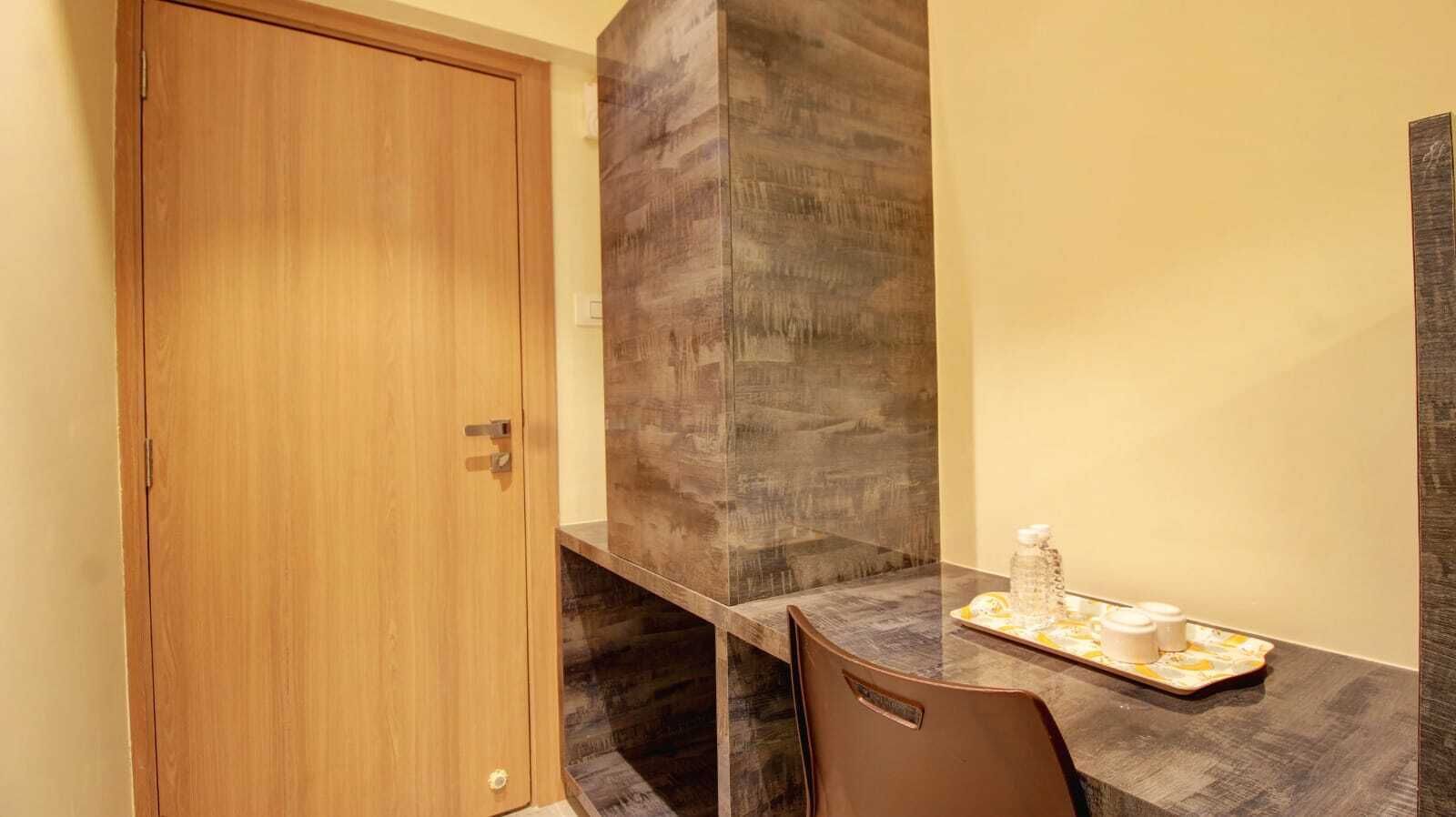 A compact room with a wooden door, a dark wood accent wall, a small table with a tray of items, and a single chair.