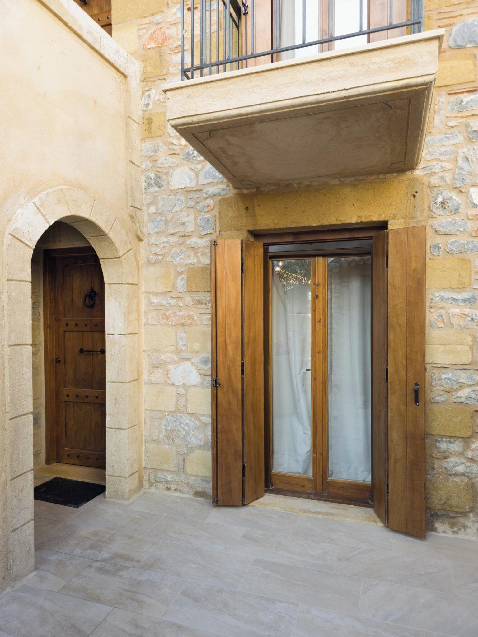 A stone building with a wooden door and a balcony with a metal railing.