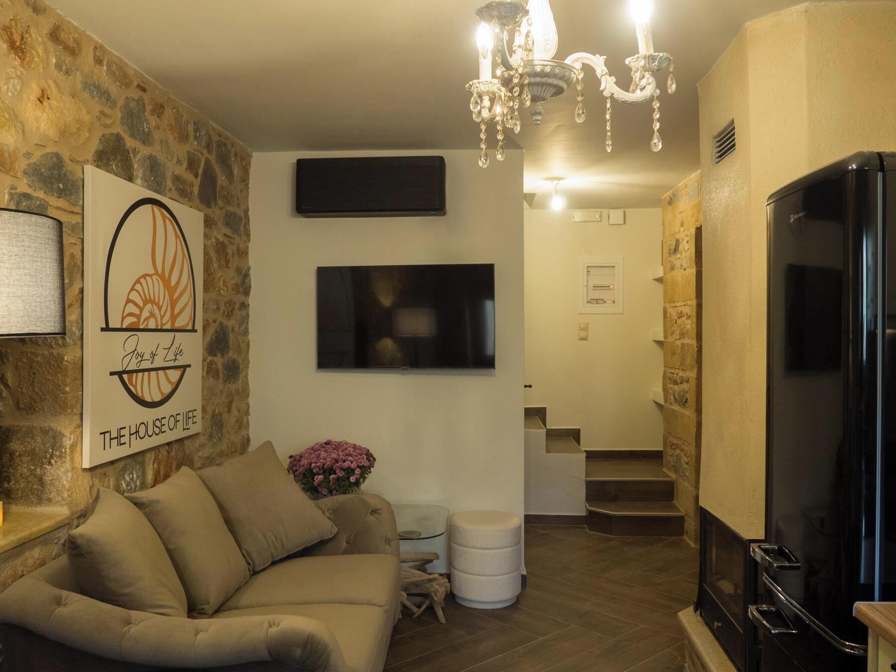 A living room with a sofa, a TV, a chandelier, and a stone wall.