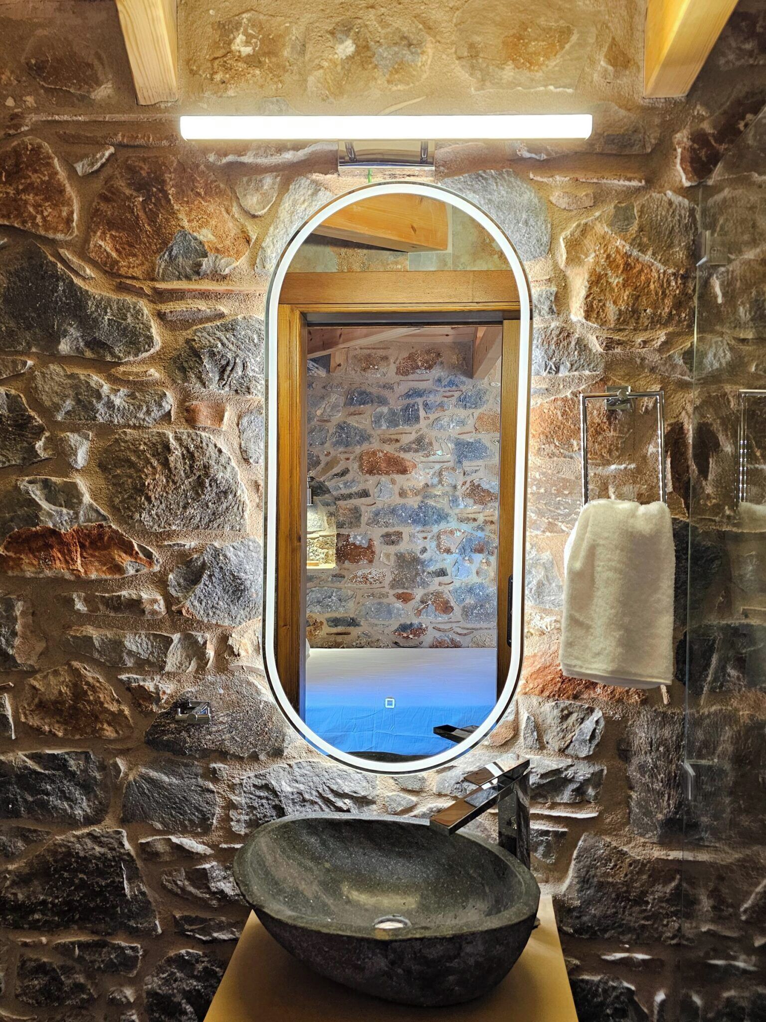 Un baño con paredes de piedra, un espejo redondo, un lavabo y un perchero para toallas.