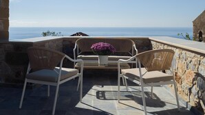 An outdoor seating area with wicker chairs and a table, overlooking a coastal view.