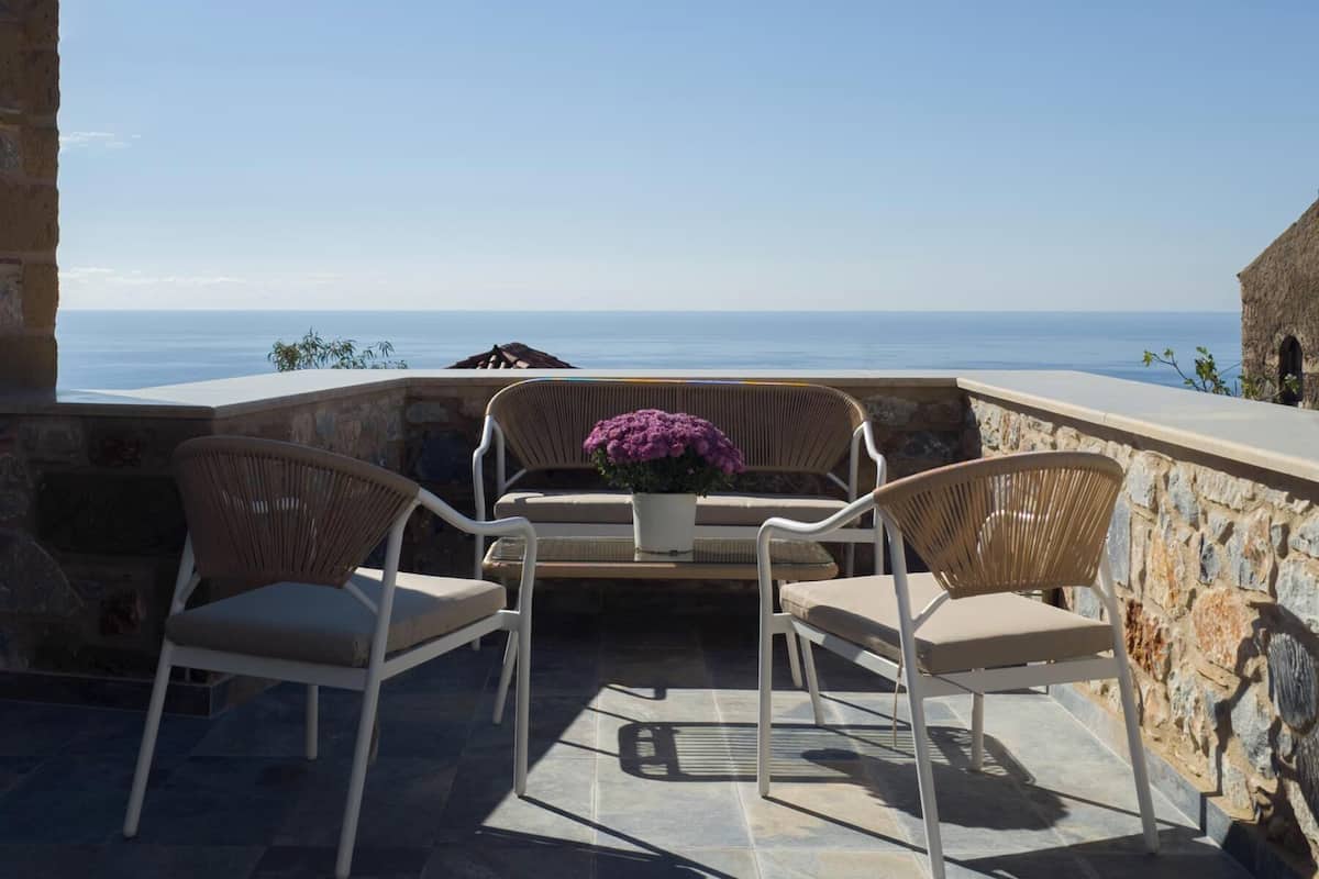 Un espace extérieur aménagé avec des chaises et une table en osier, offrant une vue sur la côte.