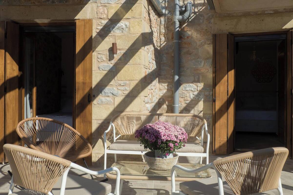 Un espace extérieur aménagé avec des chaises et une table en osier, un mur en pierre et une porte.