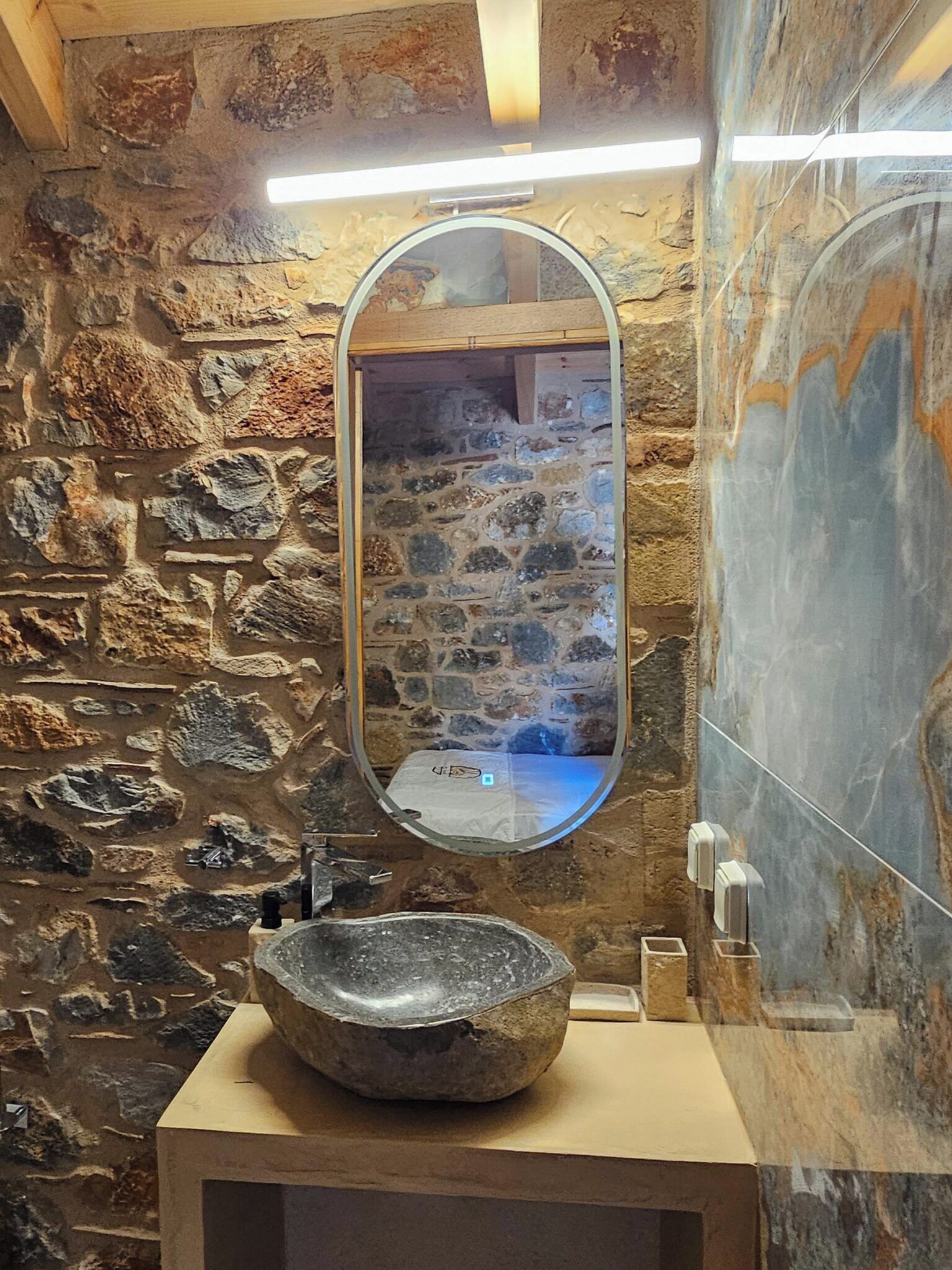 A bathroom with a stone wall, a round sink, and a mirror.