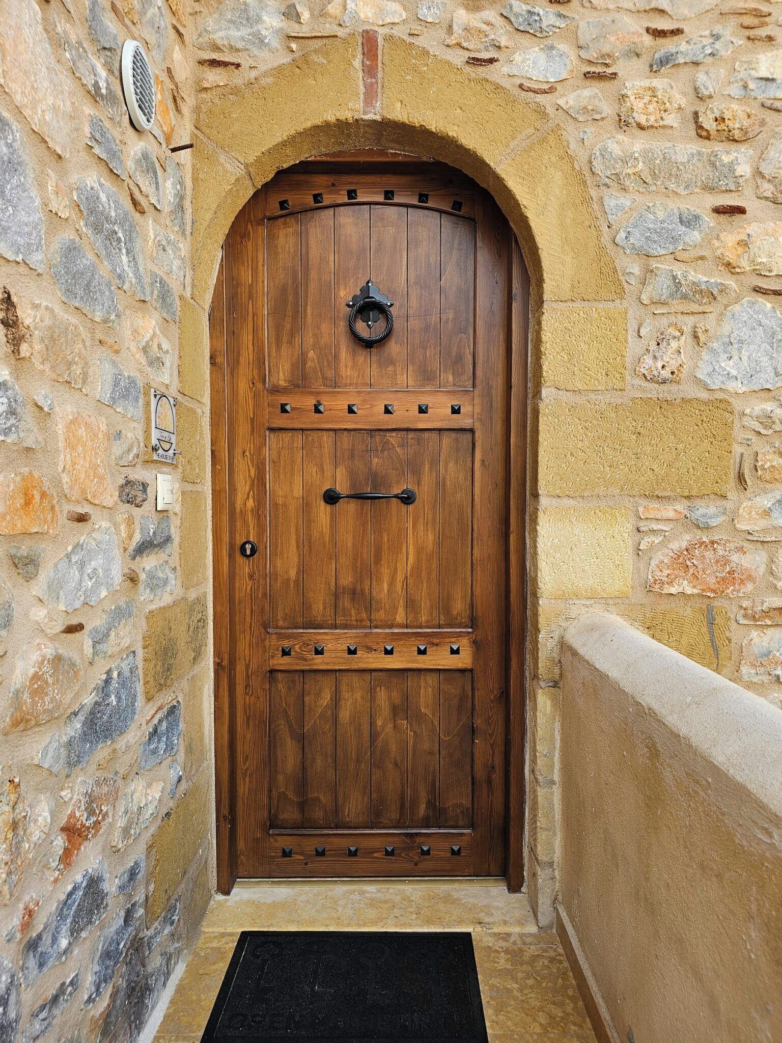 Una puerta de madera con un aldabón metálico, en una pared de piedra con un repisa de piedra a la derecha.