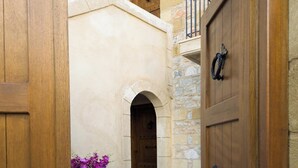 A stone building with a wooden door and a large planter with purple flowers.