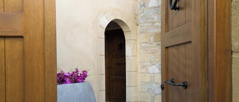 Un edificio de piedra con una puerta de madera y una maceta grande con flores moradas.