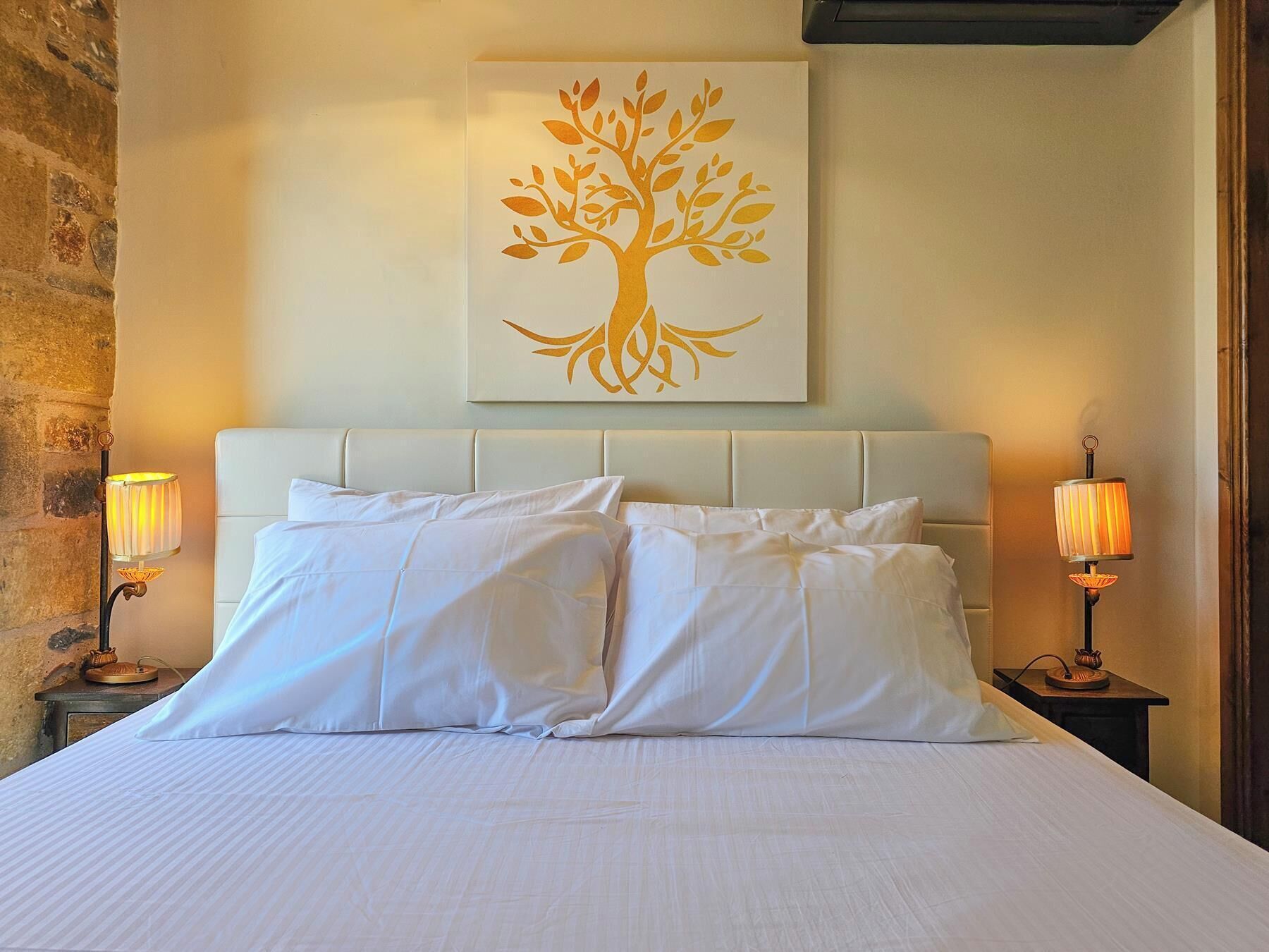 Een hotelkamer met een bed, twee bedlampjes en een kunstwerk van een boom aan de muur.