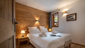 A bedroom with a wooden wall, a bed with white bedding, two bedside lamps, and a window with a view. - Wifi, 150m from ski slopes, 1st floor, balcony, parking, tv, 67m², Les Gets (Les Gets)
