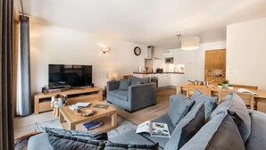 A modern living room with a grey sofa, a coffee table, and a TV. There's a kitchen area with cabinets and a microwave. - Wifi, 150m from ski slopes, 1st floor, balcony, parking, tv, 67m², Les Gets (Les Gets)