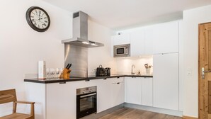 A modern kitchen with white cabinetry, a stainless steel range hood, a built-in oven, a microwave, and a wooden dining table with chairs. - Wifi, 150m from ski slopes, 1st floor, balcony, parking, tv, 67m², Les Gets (Les Gets)