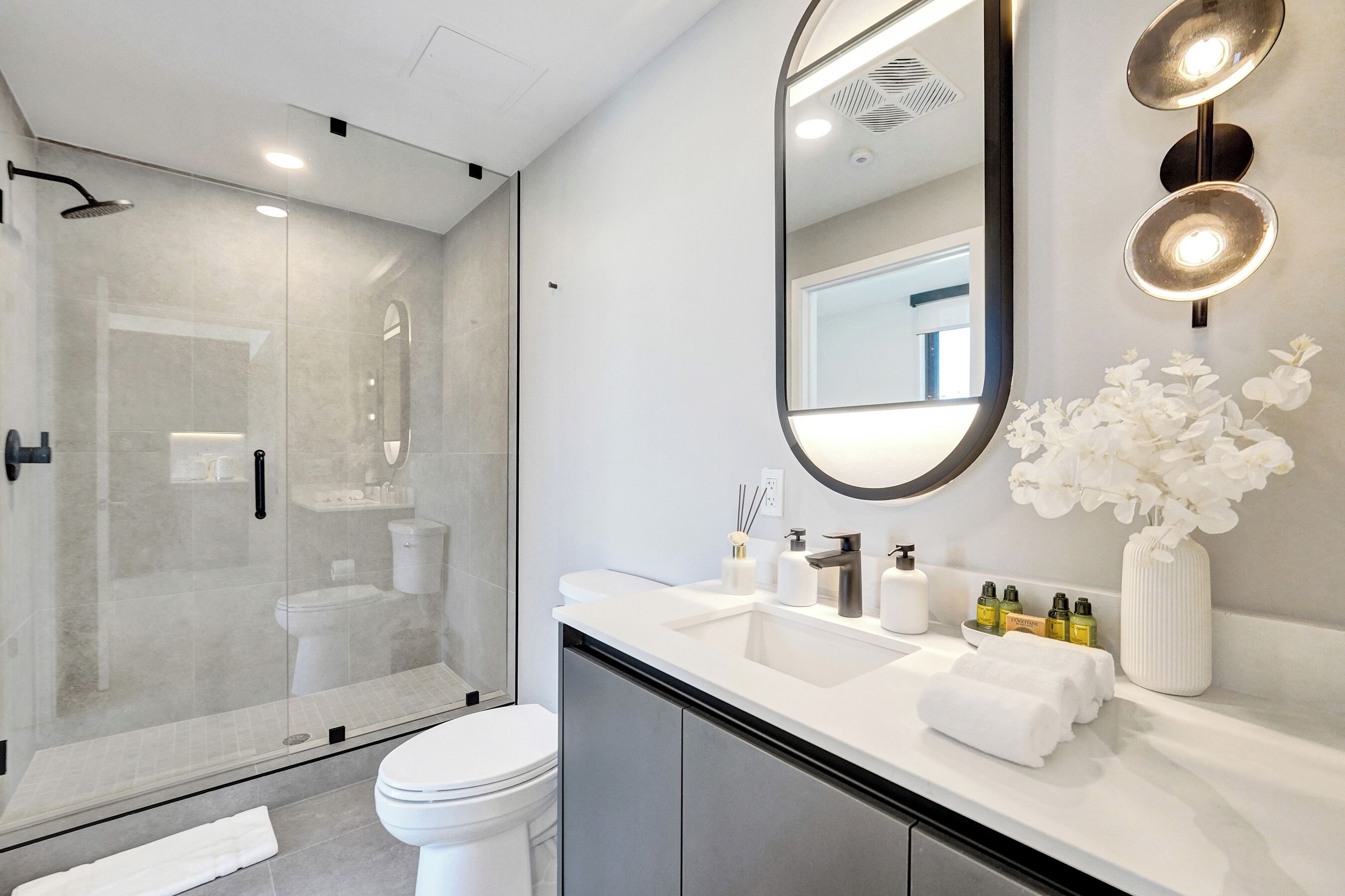 A modern bathroom with a glass-enclosed shower, a white sink, and a large mirror.