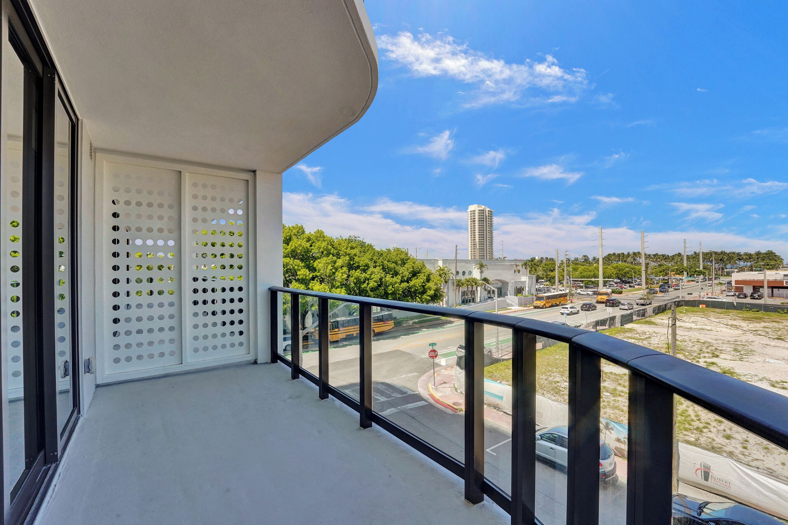 A balcony with a view of a busy street, a tall building, and greenery.