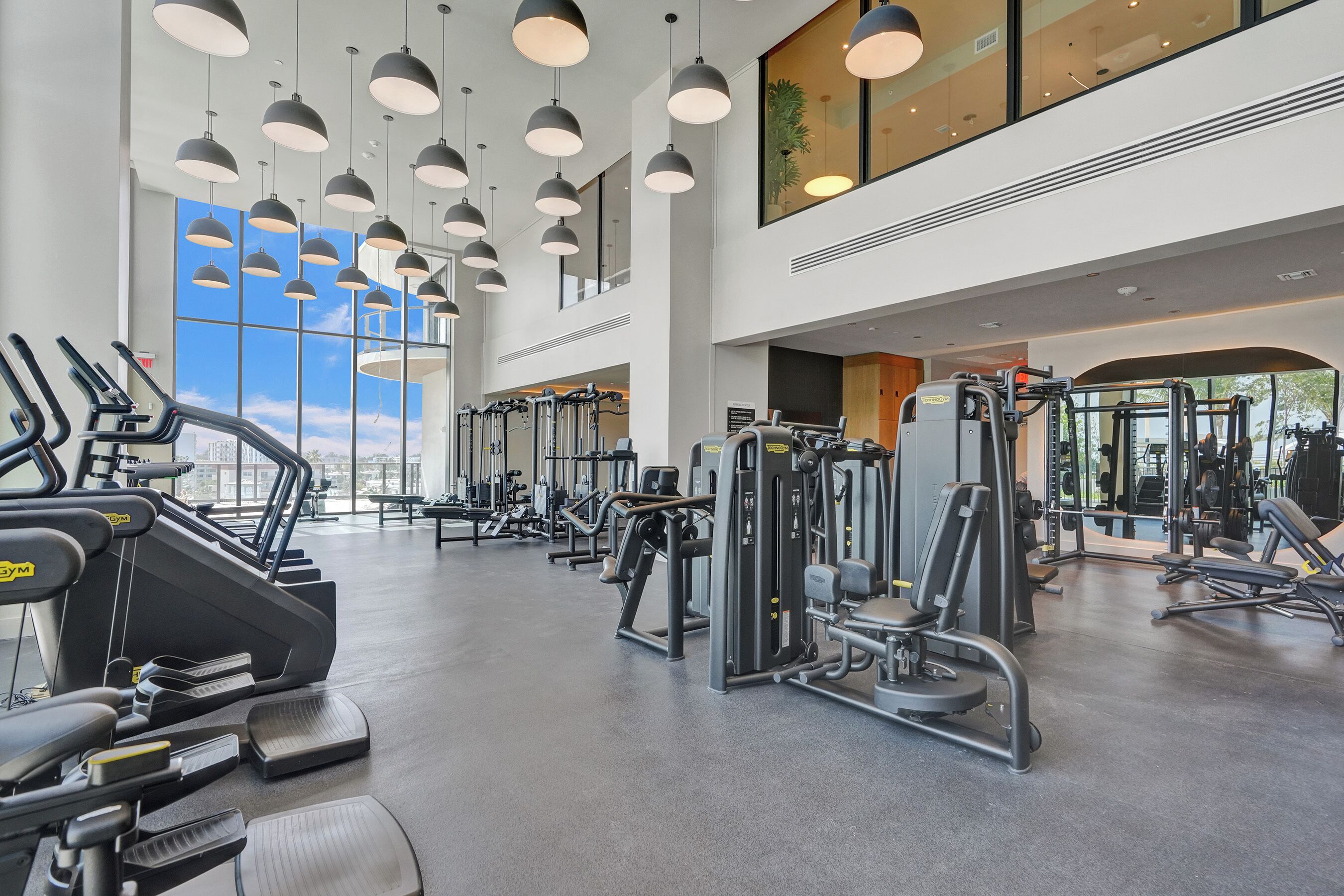 A gym with treadmills, weight machines, and a large window offering a view of the sky.