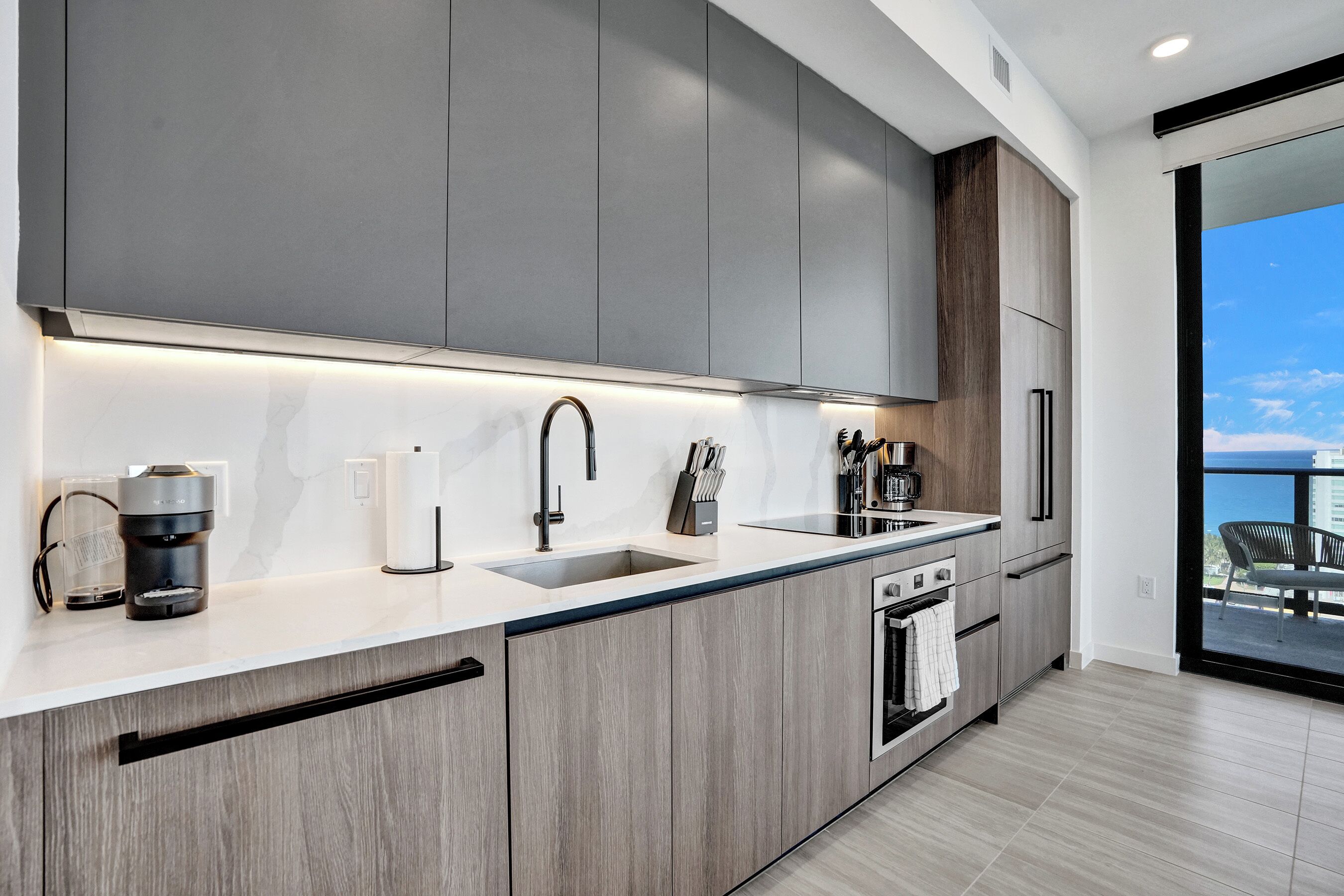 Een moderne keuken met grijze kastjes, een roestvrijstalen spoelbak en een ingebouwde oven.