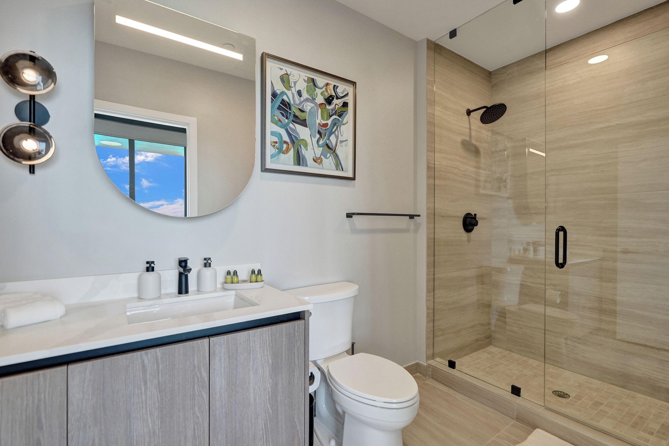 A modern bathroom with a glass-enclosed shower, a large mirror, and a sink with toiletries.