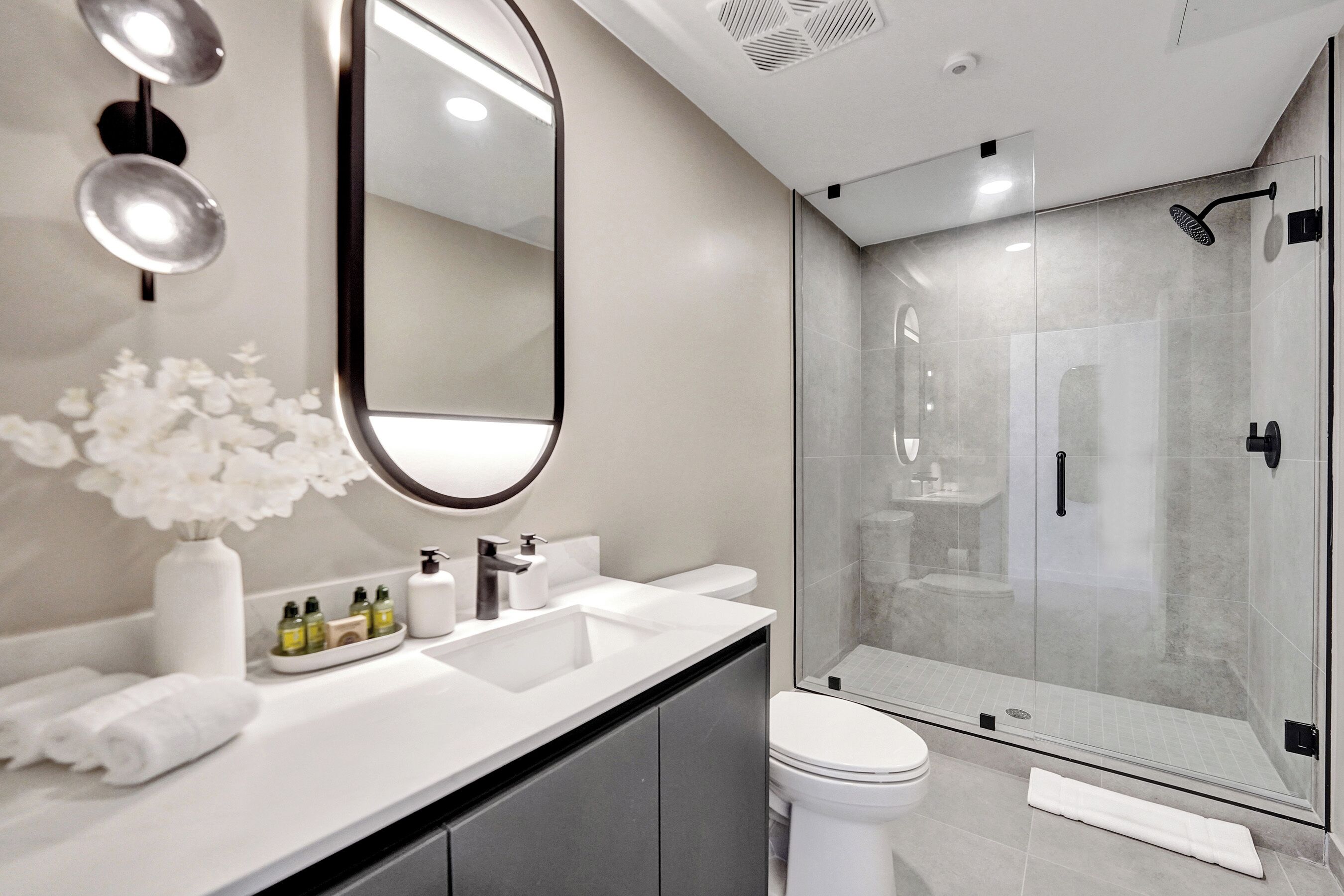 A modern bathroom with a large mirror, white sink, and a glass-enclosed shower.
