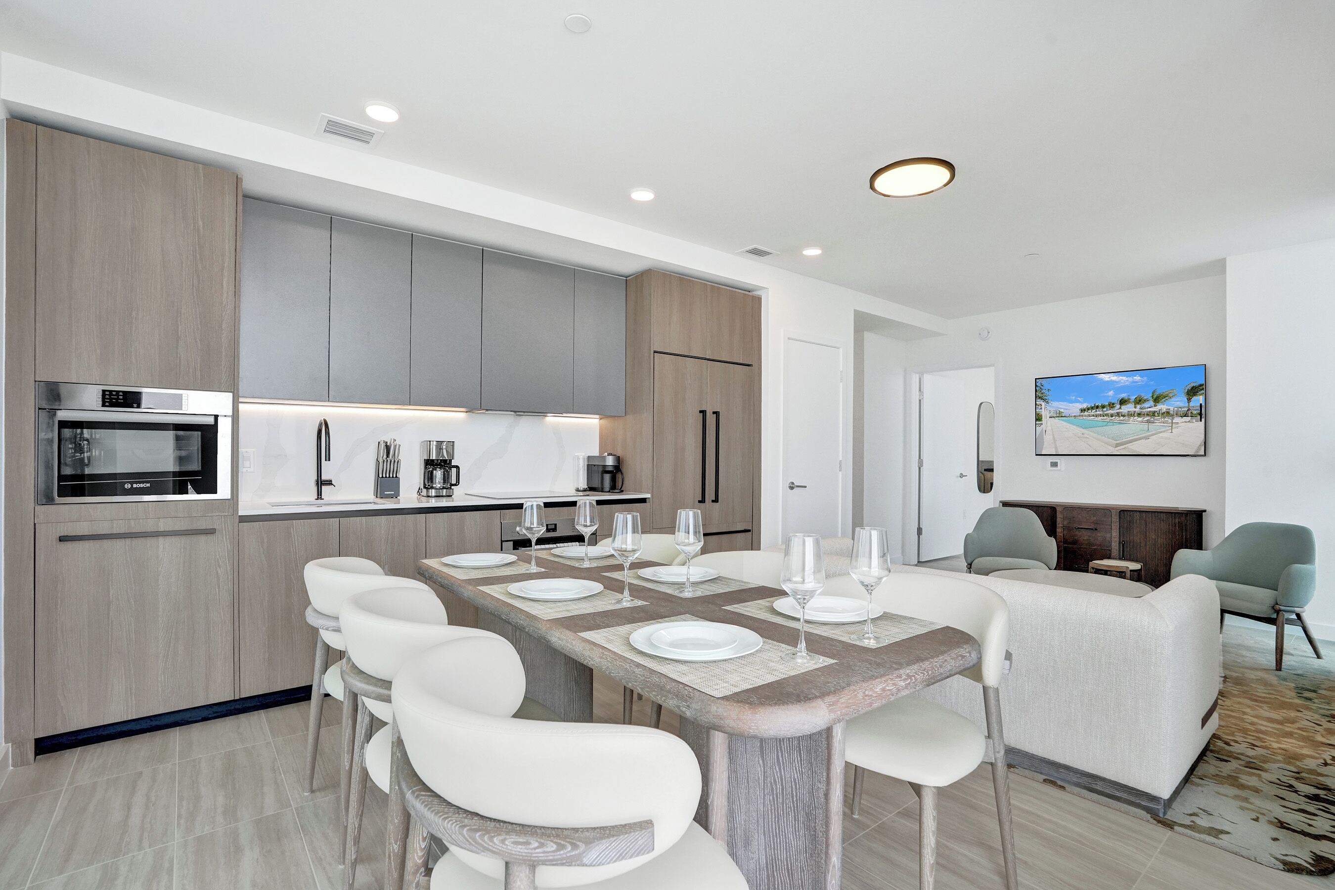 A modern kitchen with built-in appliances, a dining area with a long table and chairs, and a living area with a sofa and chairs.