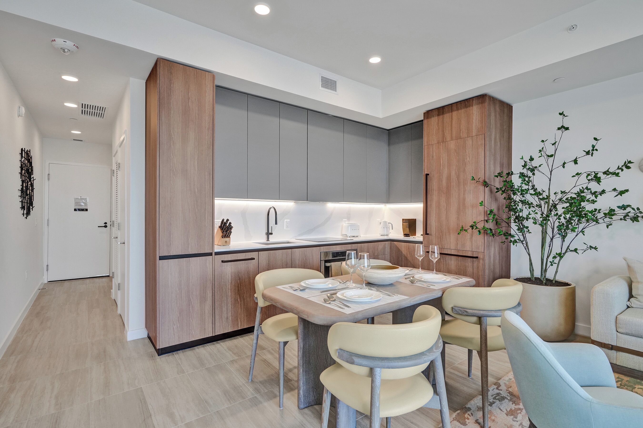 Una cocina moderna con armarios grises, una pared decorativa de madera y un comedor con mesa lista para cuatro.