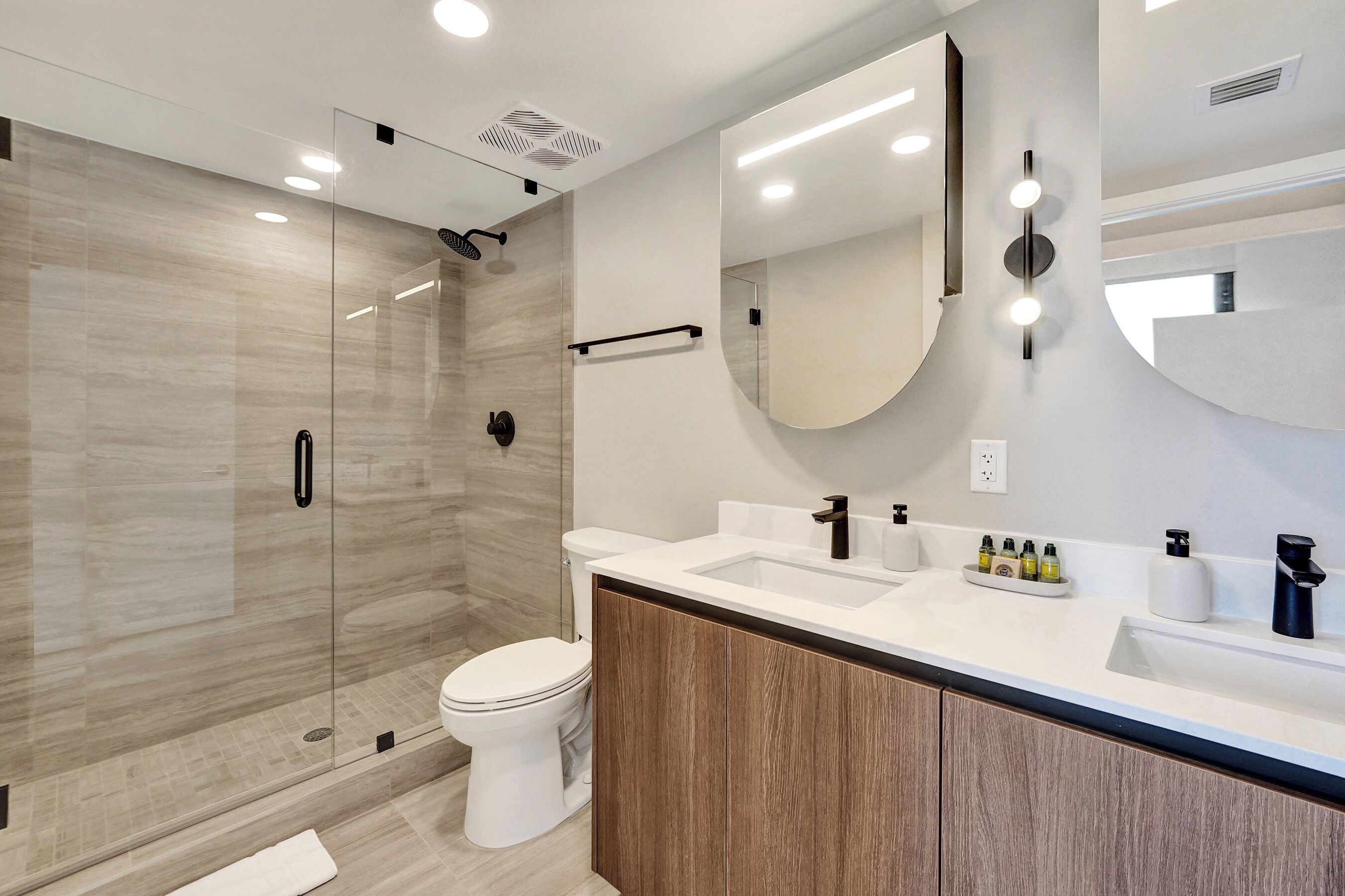 A modern bathroom with a glass-enclosed shower, a white toilet, and a vanity with a mirror and sink.