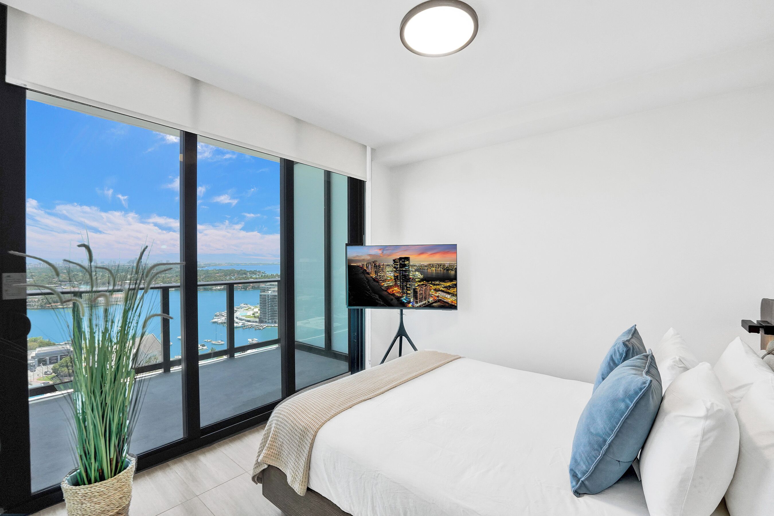 Een moderne hotelkamer met een ruim balkon, een bed met witte lakens en een flatscreen televisie aan de muur.