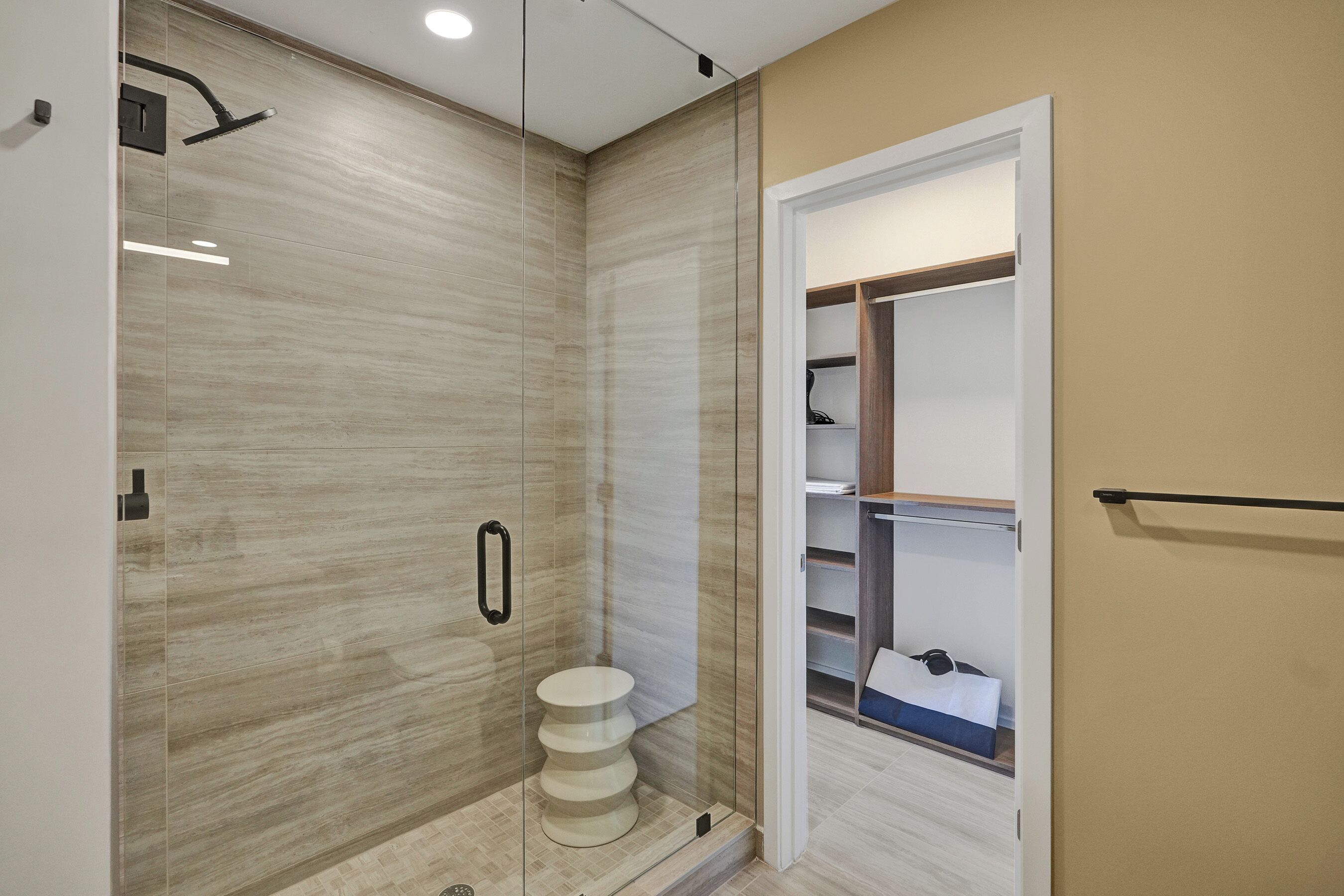 A modern bathroom with a glass-enclosed shower, a toilet, and a walk-in closet with shelves.
