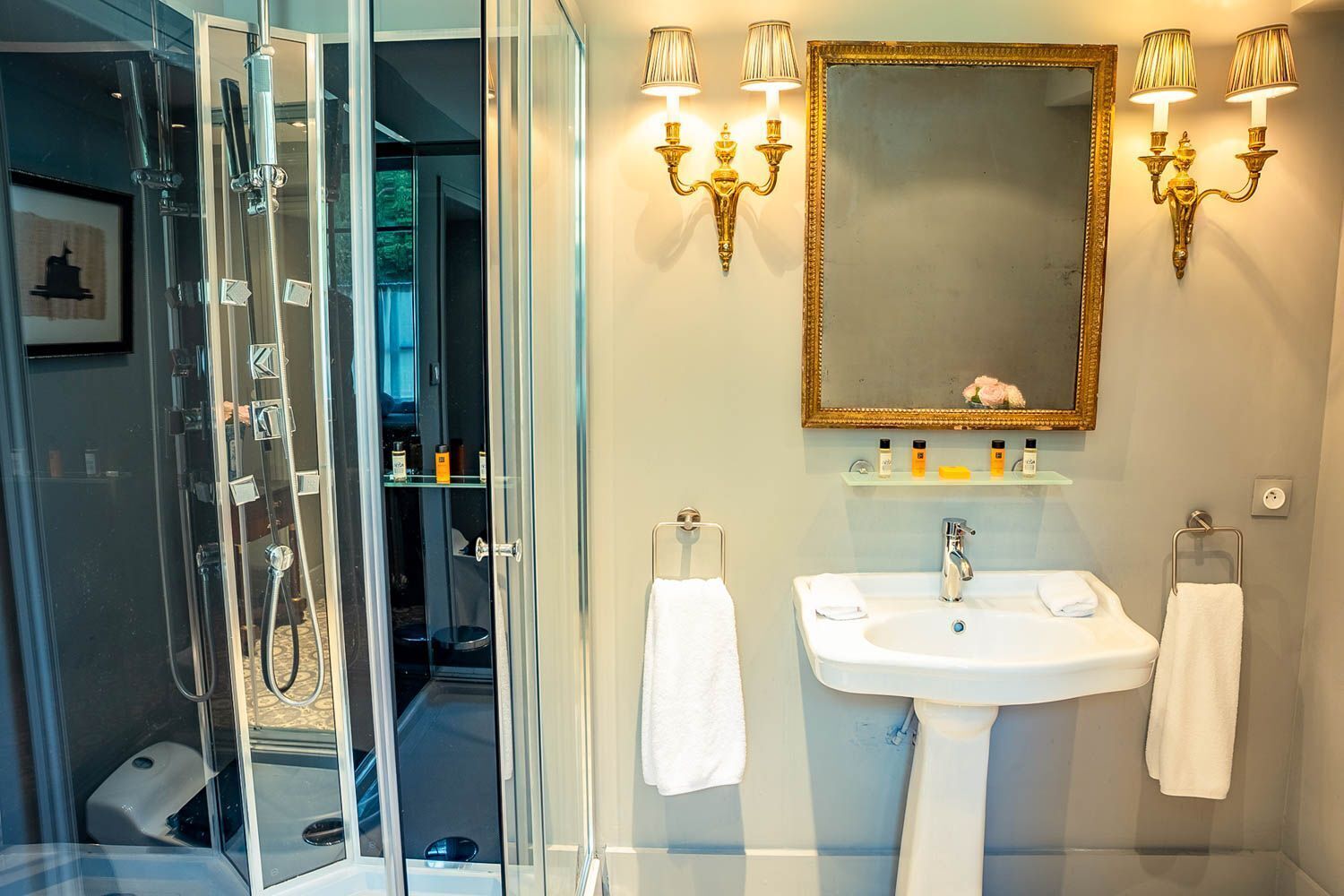 A modern bathroom with a glass-enclosed shower, a white sink, and a large mirror with wall sconces.