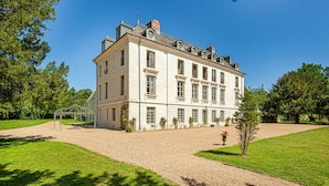 A large, multi-story building with a symmetrical facade, large windows, and a gravel driveway.