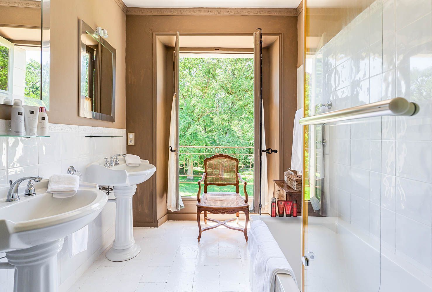 Un baño con una ventana grande, una silla de madera, una bañera y un lavamanos.