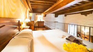 Une chambre avec un plafond en bois, un lit, une table de chevet, une lampe, une fenêtre et un escalier menant à un étage supérieur.