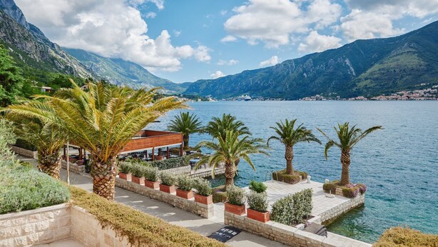 Un hôtel situé sur la côte, doté d’une terrasse, de palmiers et offrant une vue sur la mer et les montagnes.