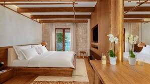 Une chambre moderne avec un lit en bois, une télévision et un balcon doté d’un mur en pierre.