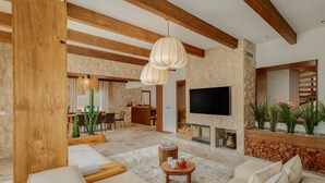 Un salon spacieux avec un grand canapé, une table basse et une cheminée. Un téléviseur est fixé au mur, et on aperçoit un coin repas au fond de la pièce.