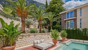 Un espace aménagé au bord de la piscine, avec une terrasse en bois, un canapé blanc et des plantes en pot.