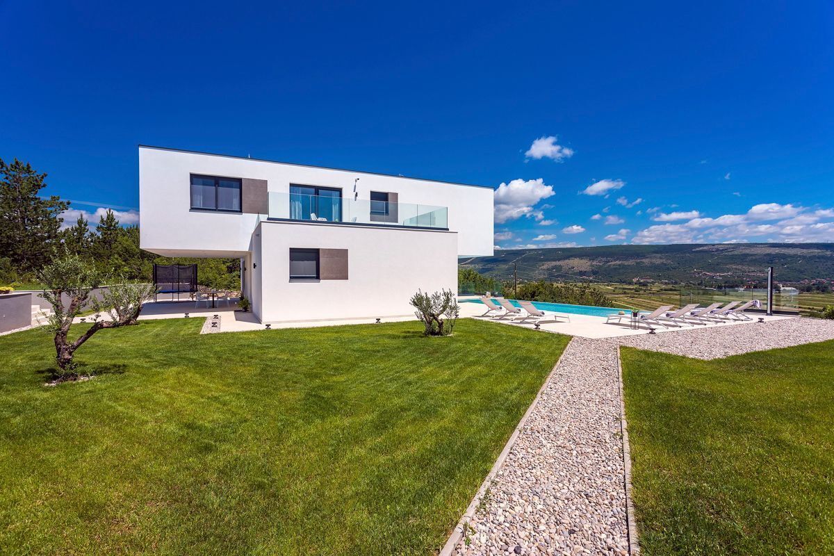 Ein modernes, zweistöckiges Haus mit Swimmingpool, gepflegtem Rasen und freiem Blick auf die umliegende Landschaft.
