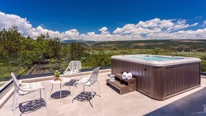 Eine Dachterrasse mit Whirlpool, zwei Stühlen, einem Tisch und Blick auf die Landschaft.