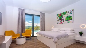 Ein modernes Schlafzimmer mit einem großen Bett, zwei gelben Sesseln, einem weißen Schreibtisch und einem großen Fenster mit Vorhängen.