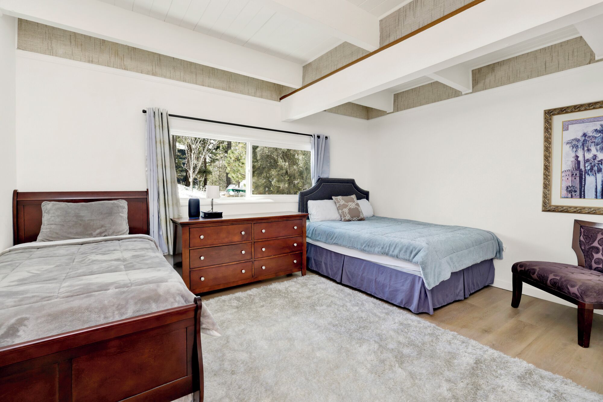 A bedroom with two beds, a dresser, a chair, and a window with a view of trees.