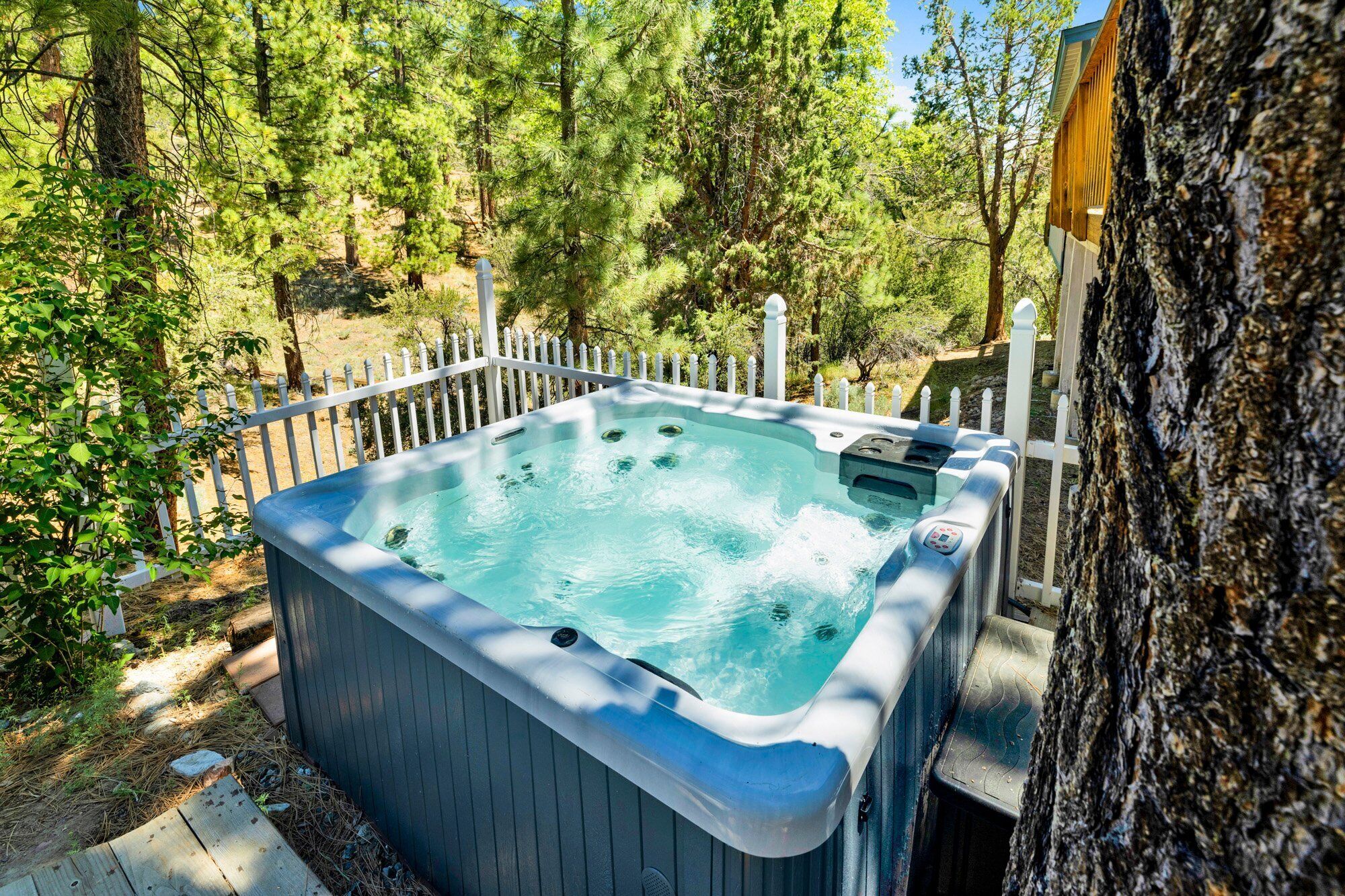 A hot tub in a wooded area with a white fence.