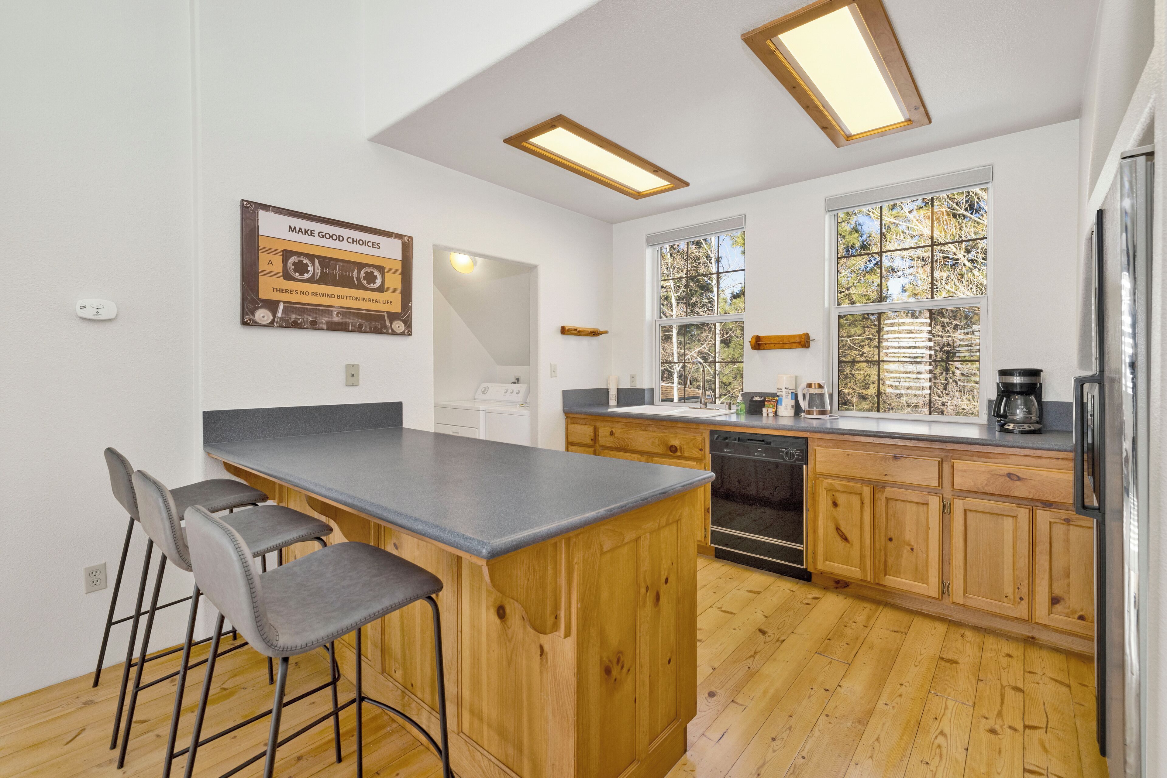 A modern kitchen with a central island, bar stools, wooden cabinets, and a large window providing natural light.