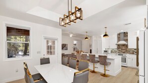 Een moderne keuken met witte kasten, een centraal eiland en een eetgedeelte met een witte tafel en grijze stoelen.