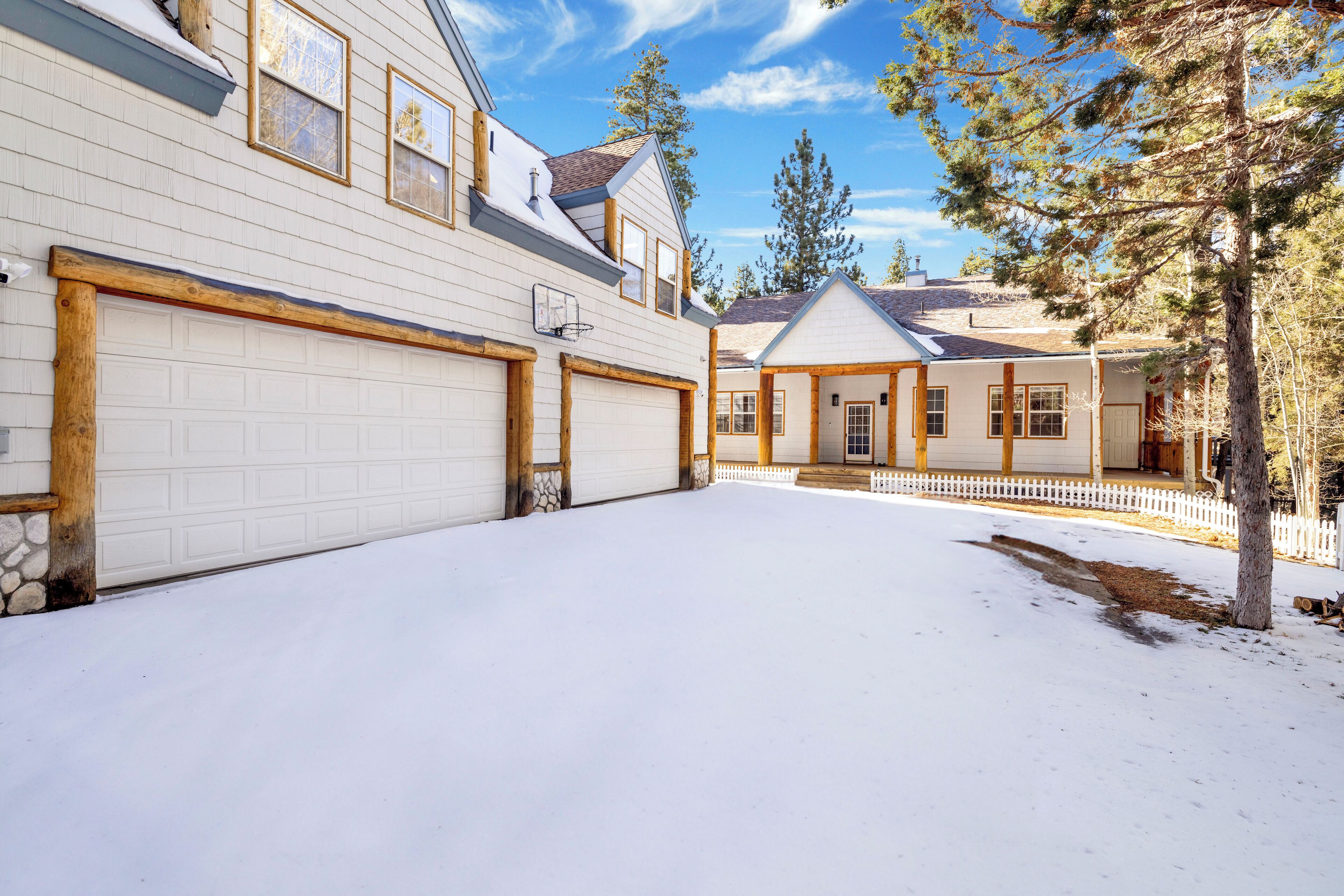 A snow-covered driveway leading to a two-story house with a garage, a covered porch, and a stone foundation.