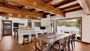 A spacious kitchen with white cabinets, a central island, and a large dining area with wooden chairs and a table. - Bear Lake Lodge #2547 (Big Bear Lake)