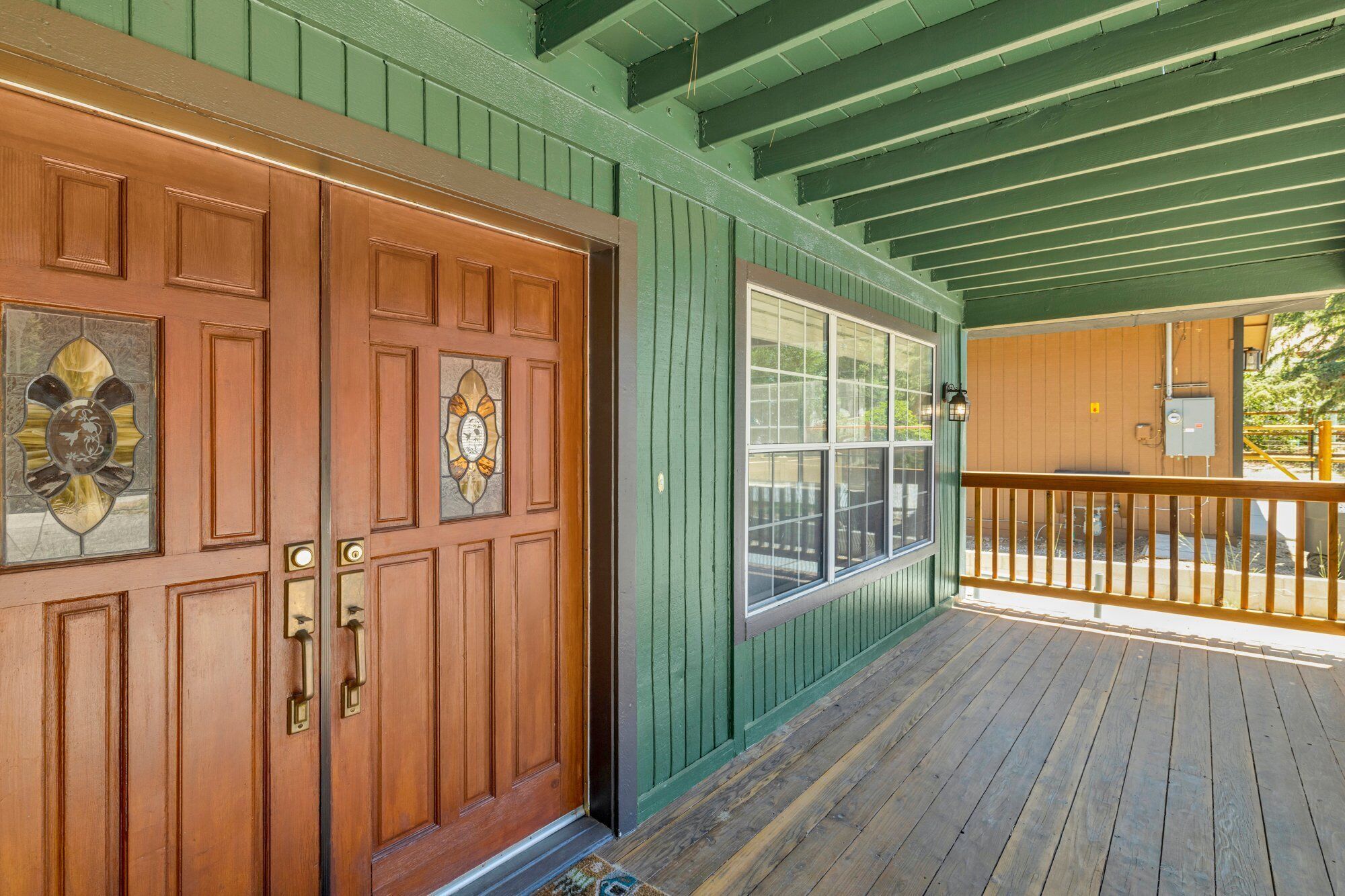 Una puerta de madera con paneles de vidrio y una pared exterior verde.