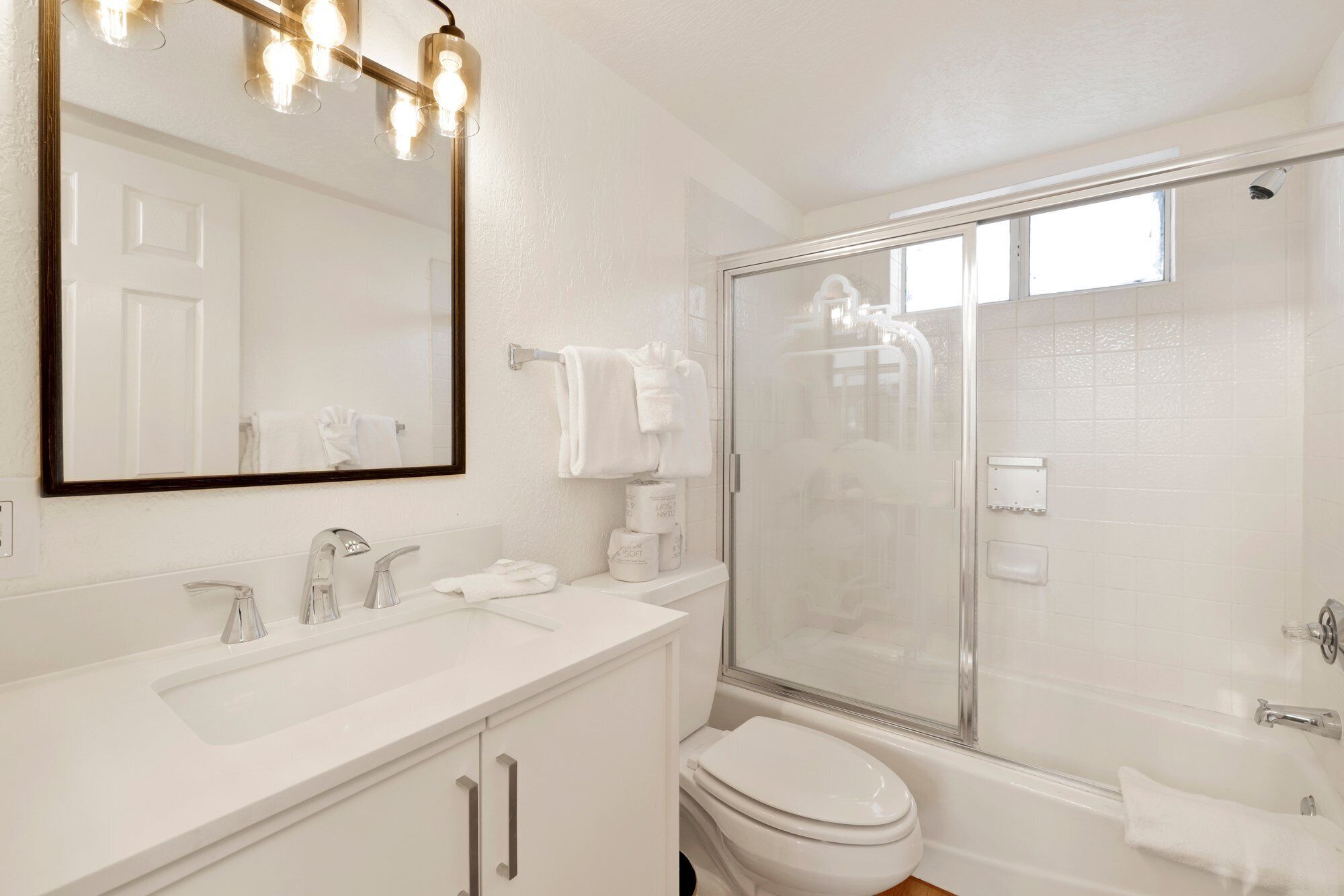 A bathroom with a large mirror, two sinks, a toilet, and a glass-enclosed shower.