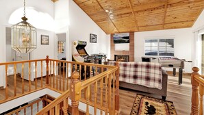 Una sala de estar amplia con un techo alto de madera, una chimenea, una mesa de fútbol y un sofá acogedor.
