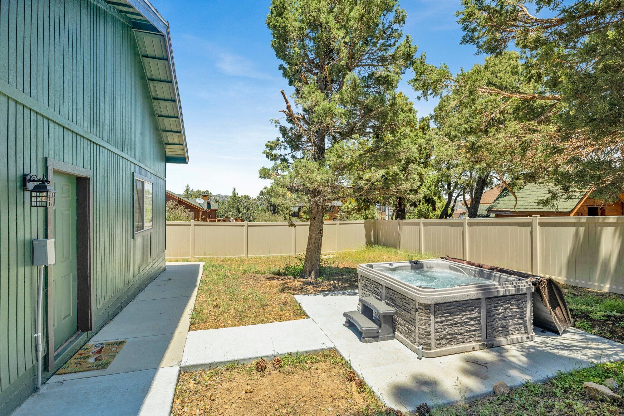 A backyard with a hot tub, a wooden deck, and a house with a green exterior.