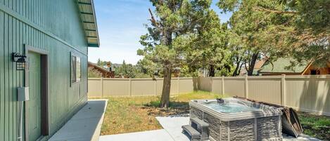 A backyard with a hot tub, a wooden deck, and a house with a green exterior.