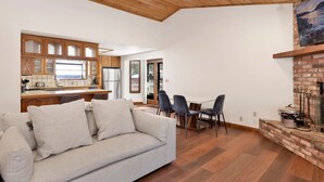 Una sala de estar moderna con techo de madera, un sofá, una mesa de comedor con sillas y una chimenea.