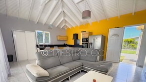 A modern living room with a grey sectional sofa, a white coffee table, and a kitchen area with appliances and a yellow wall. - Villa Perrin Évasion à 9 min de l'aéroport de la Guadeloupe (Les Abymes)